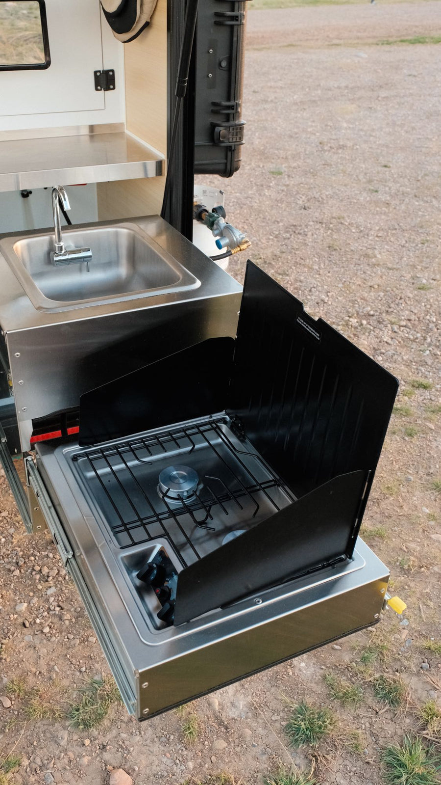 ideal for outdoor adventures in nature.|Experience an RV rental adventure! A rugged off-road camper trailer sits silhouetted against a golden sunset in a natural landscape.|This rugged Boreas XT off-road camper trailer with an open door showing its interior is perfect for an RV rental adventure.|RV rental outdoor kitchen features a pull-out stainless steel sink and gas stove with wind guards for campsite cooking.|Explore with this Boreas XT overland trailer for your next RV rental adventure. Ready for off
