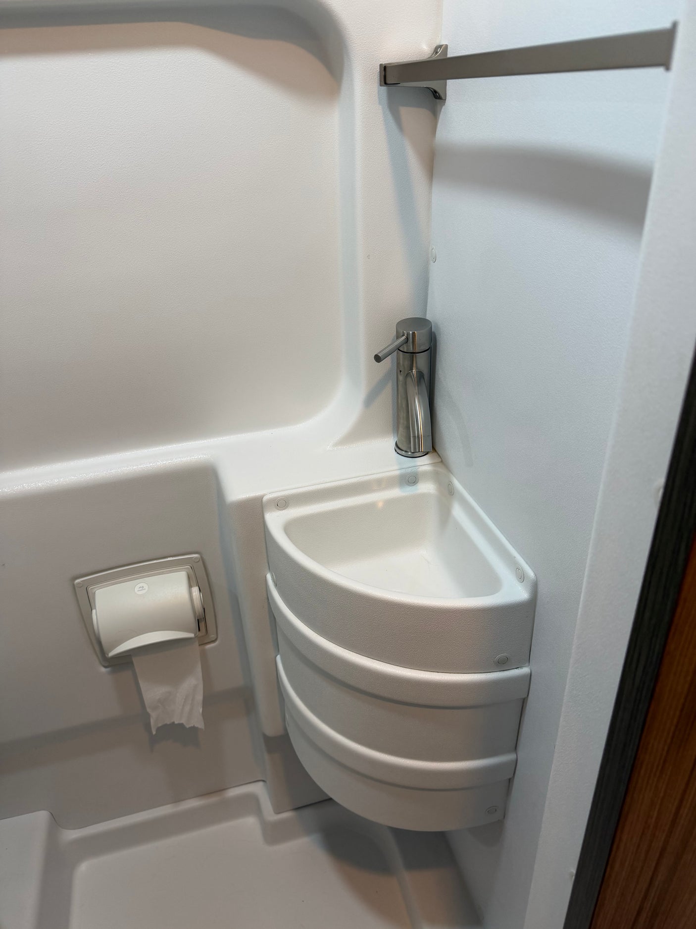 An RV rental compact wet bath. White interior with corner sink, modern faucet, and toilet paper holder, ideal for small spaces.
