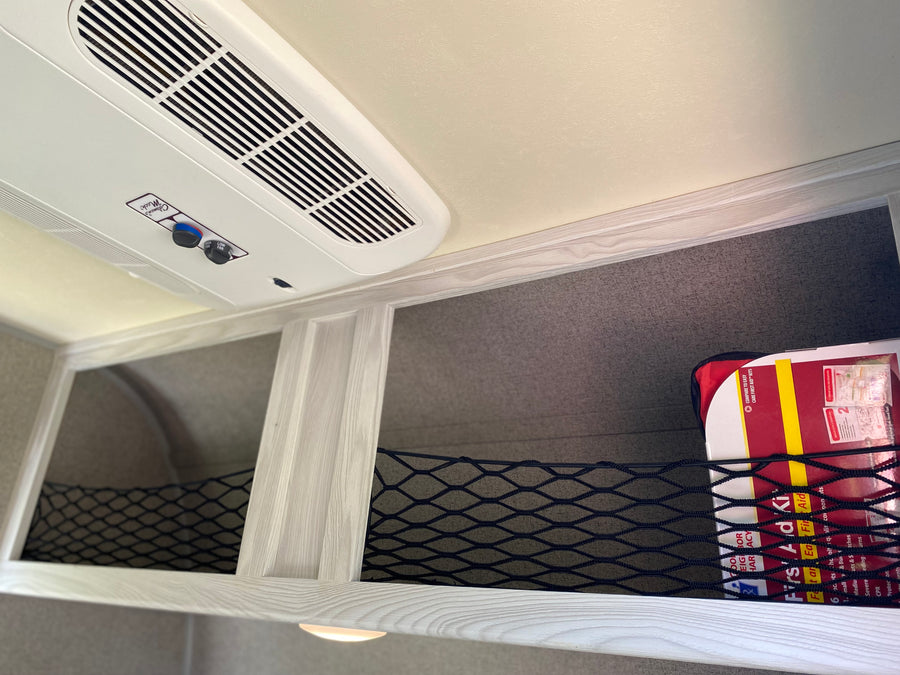 RV rental ceiling with Coleman Mach AC, overhead storage nets, and a visible first aid kit.