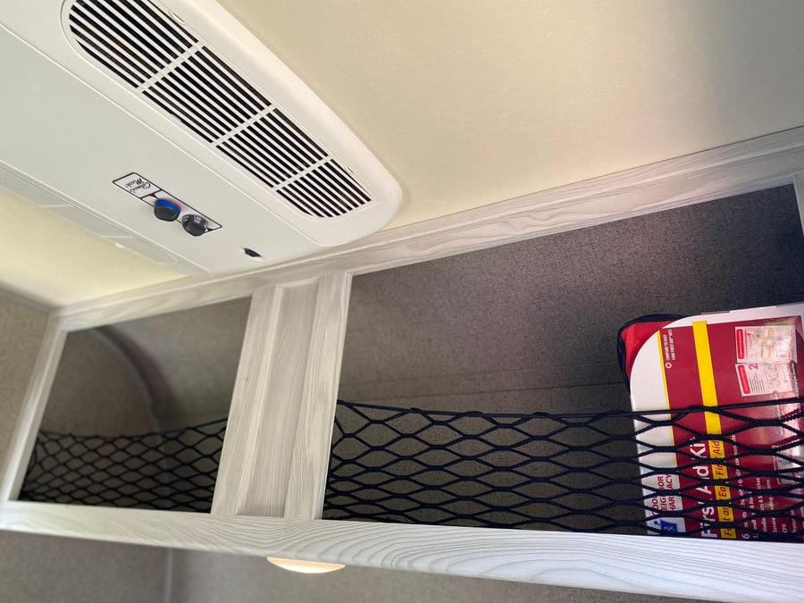 RV rental ceiling with Coleman Mach AC, overhead storage nets, and a visible first aid kit.