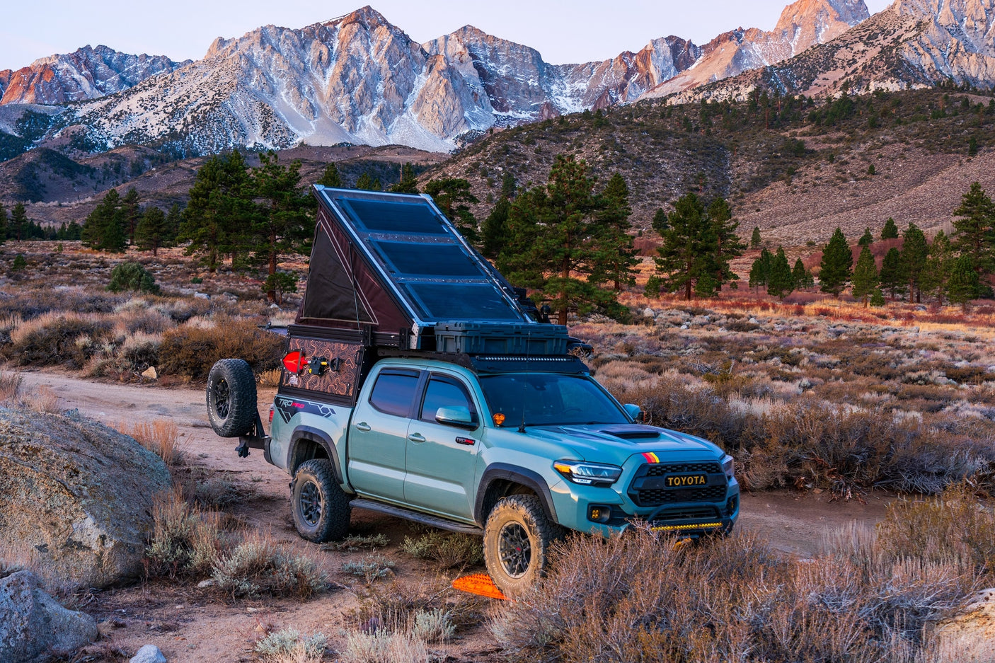 A customized overlanding Toyota Tacoma with a pop-up camper, perfect for an RV rental mountain adventure.