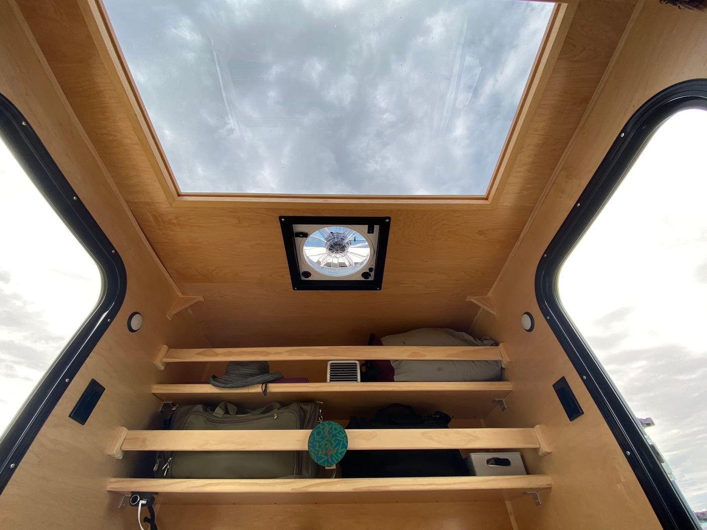 Compact RV rental interior featuring a large overhead skylight, ceiling fan, and practical storage shelves for gear.