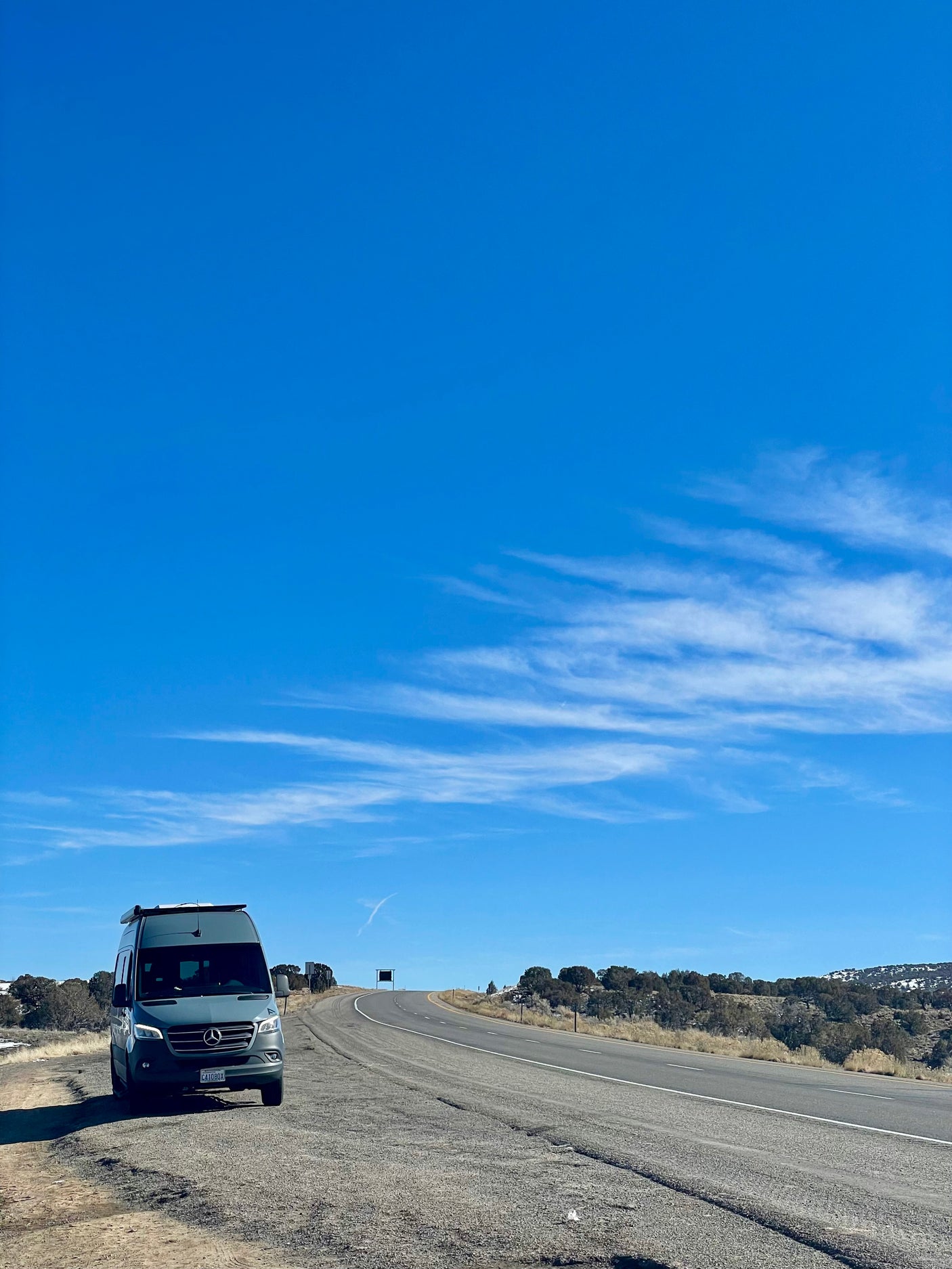 A grey Mercedes-Benz Sprinter rv rental parked by a rural highway, ready for adventure under a clear blue sky.