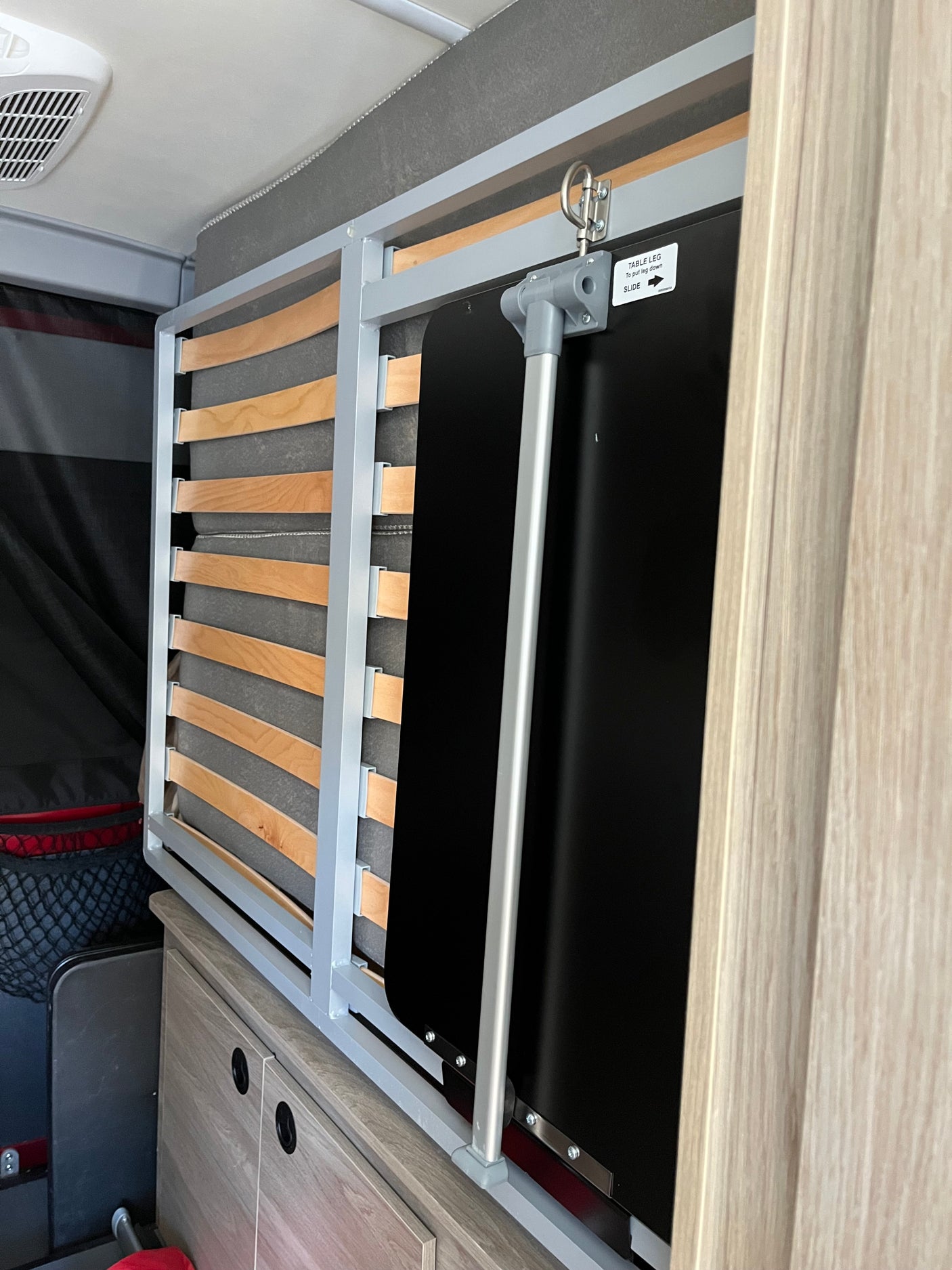 RV rental interior shows a folded bunk bed frame and a table leg mechanism, optimizing space for travel adventures.