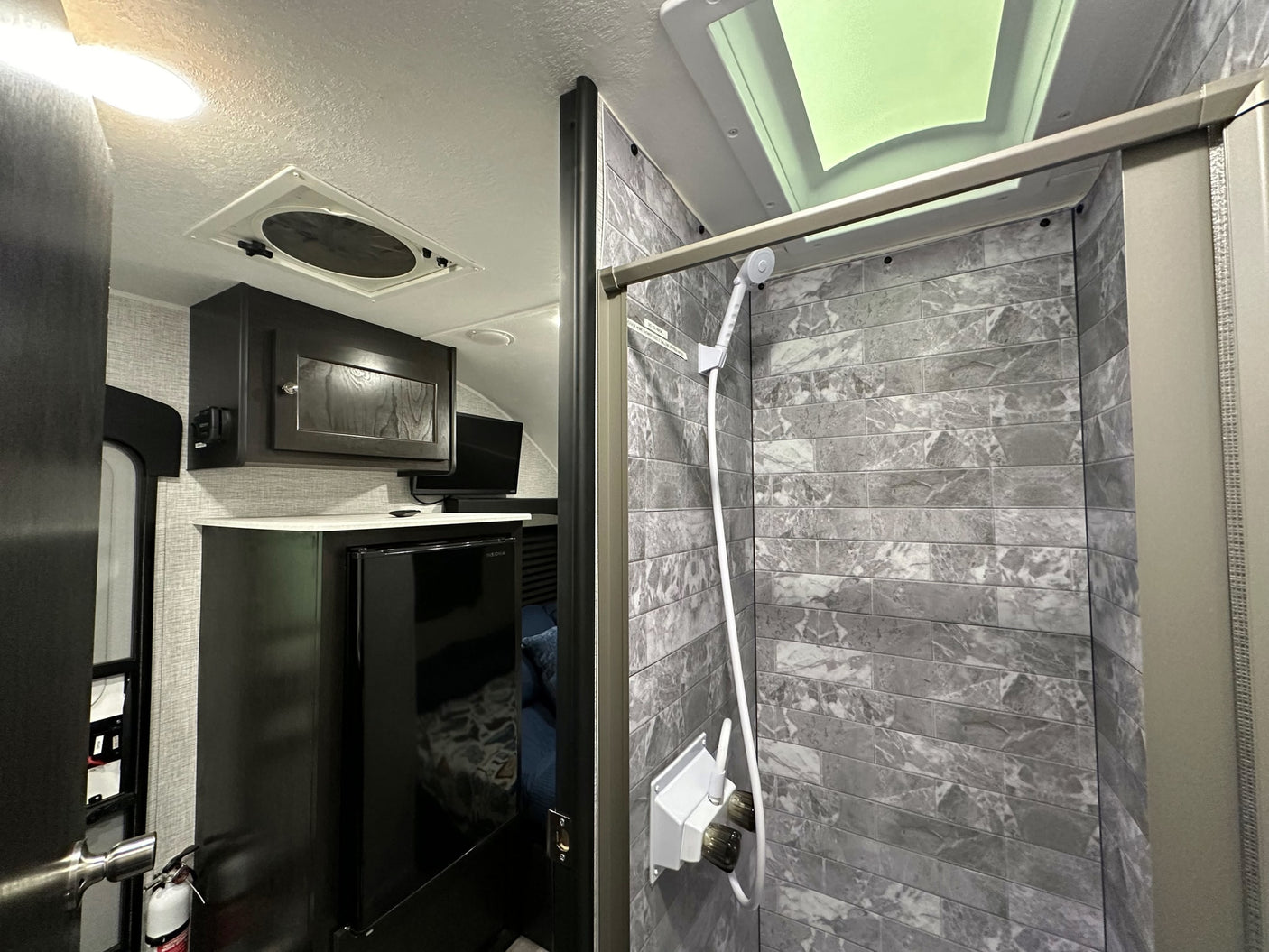 Compact RV rental interior featuring a modern kitchen area with a fridge and TV, plus a tiled shower stall with skylight.
