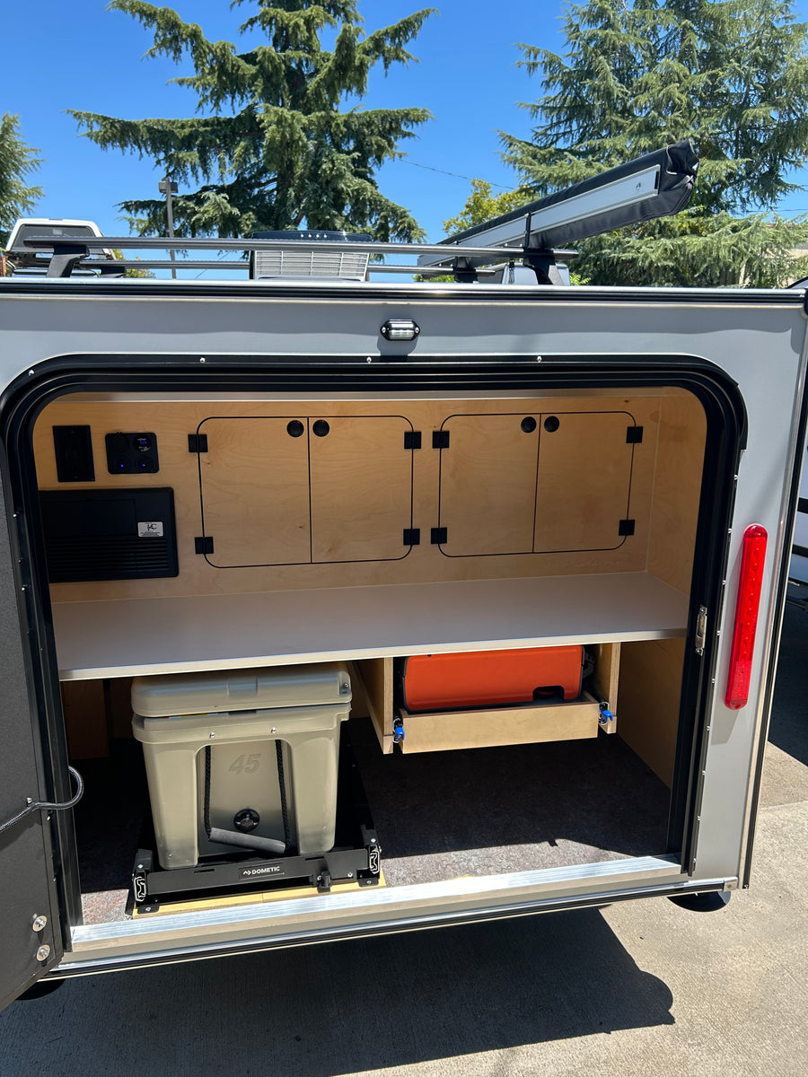 A detailed view of an rv rental's outdoor kitchen, featuring a Dometic cooler, slide-out storage, and wooden cabinets.