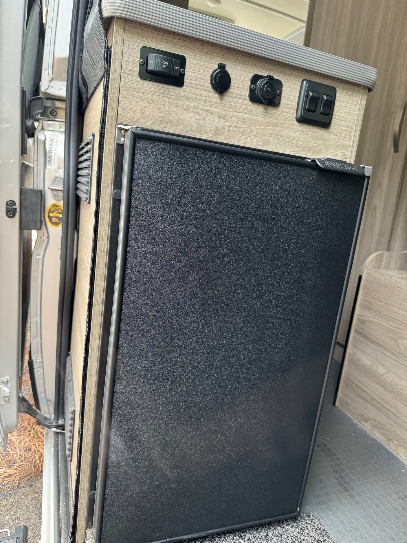 rv rental interior: compact black fridge, power outlets, and a panel with a coach battery switch.