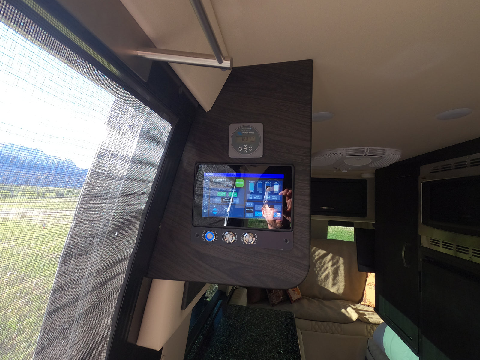 RV rental interior: A detailed view of a smart control panel, Victron Energy monitor, and sunny window with mountains.