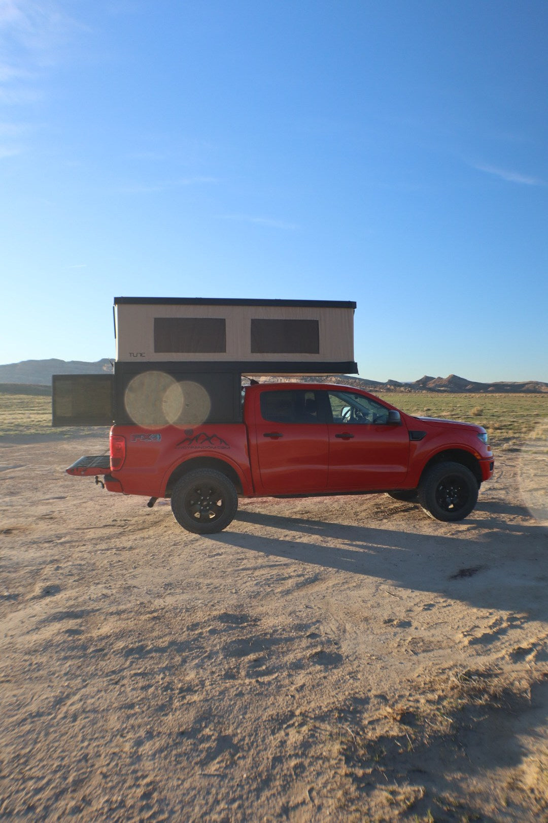 dry landscape.|A red Ford Ranger truck with a black TUNE truck camper is on a dirt road. Explore the desert with this unique RV rental!|Red pickup with TUNE truck camper