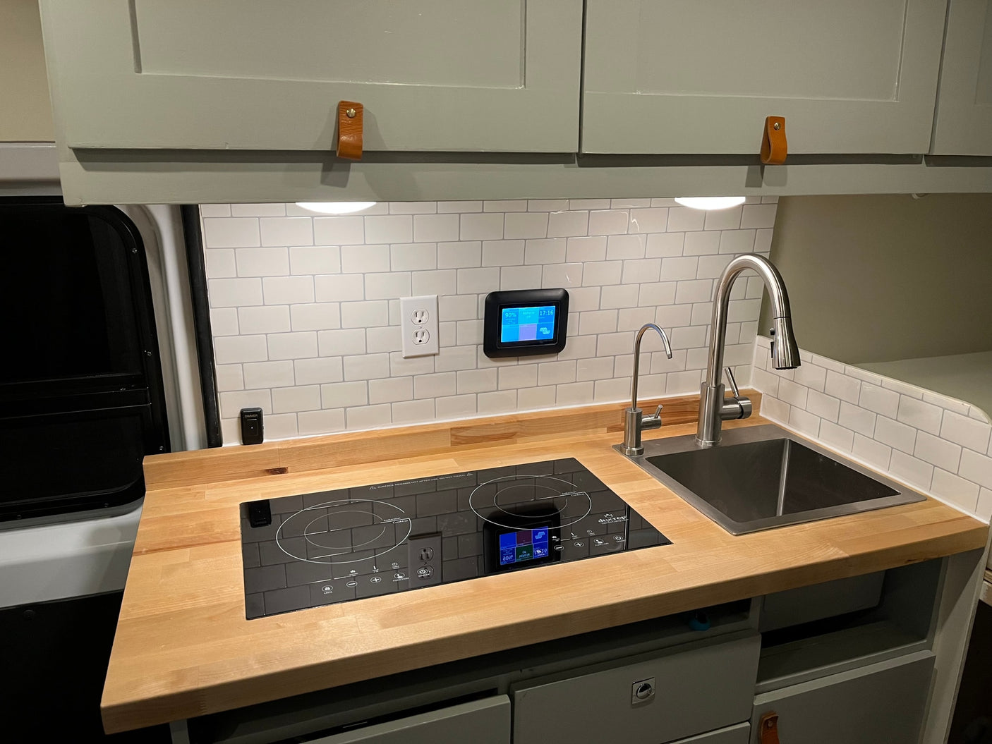 RV rental kitchen with wood counters, induction cooktop, sink, subway tile backsplash & smart system display.