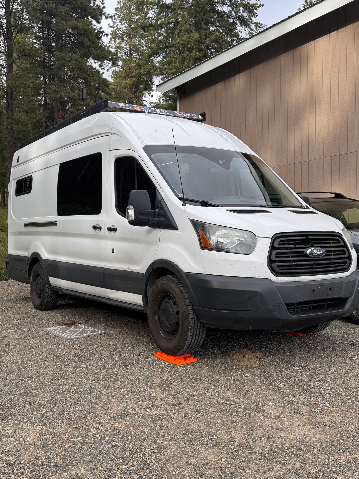 White Ford Transit rv rental campervan, parked on a gravel lot with orange leveling blocks under its tires.