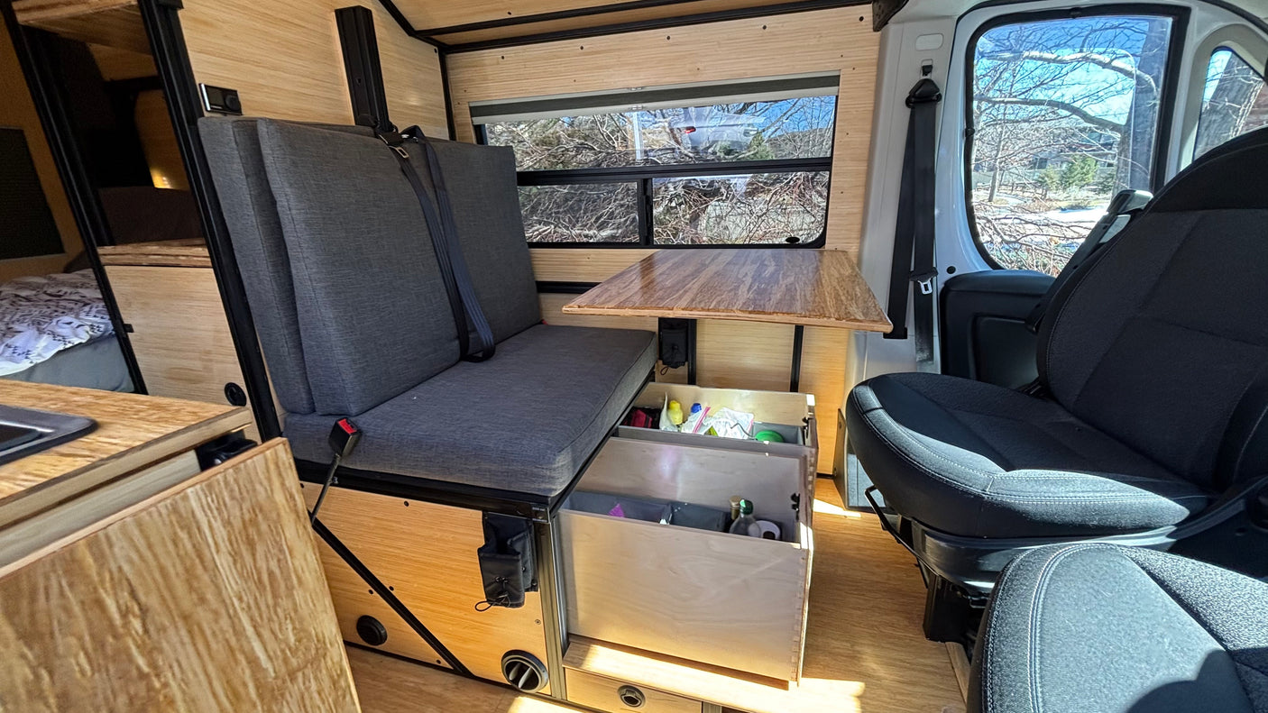 RV rental interior: Custom wood-paneled camper with a comfy bench seat, table, and practical storage drawers.