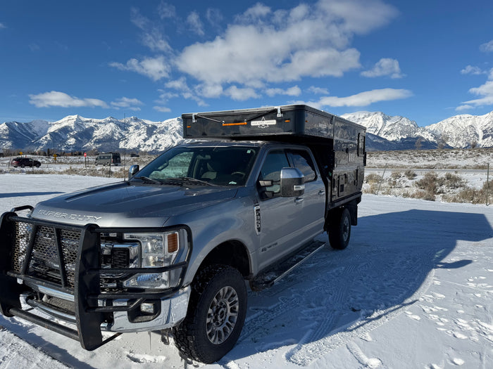 Silver Ford Super Duty truck featuring a Four Wheel Camper, parked in a snowy mountain scene. Great rv rental option!