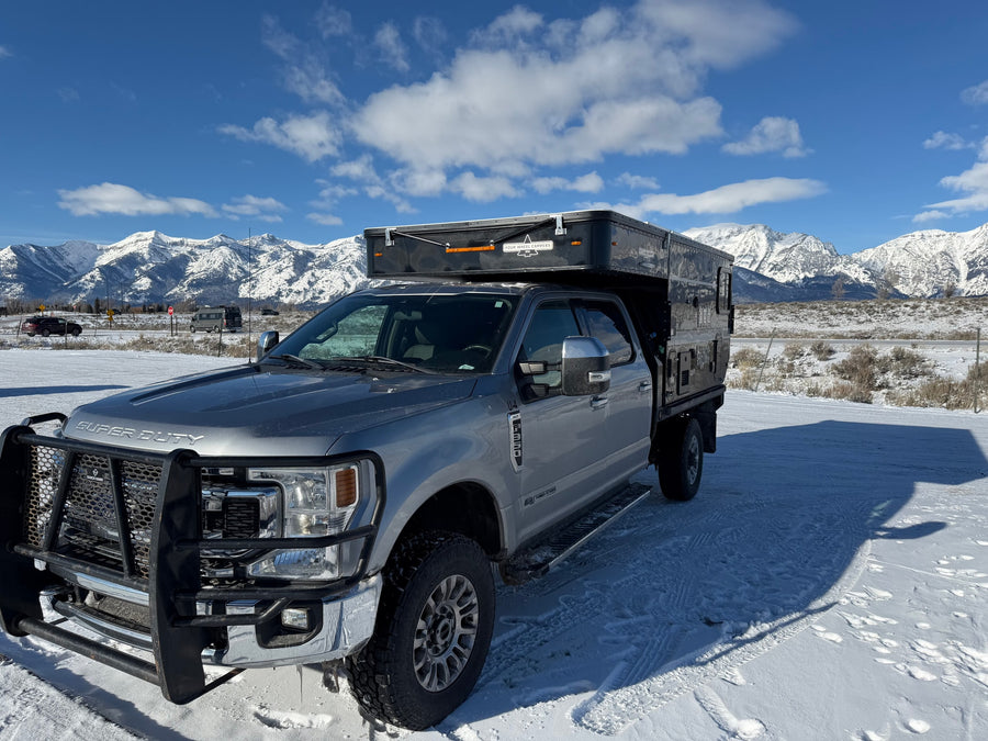 Silver Ford Super Duty truck featuring a Four Wheel Camper, parked in a snowy mountain scene. Great rv rental option!