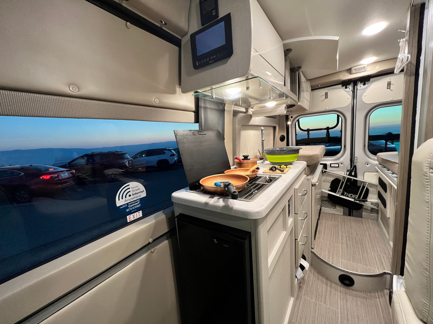 Modern RV rental interior: well-equipped kitchen with stovetop, sink, utensils, and scenic mountain views outside.