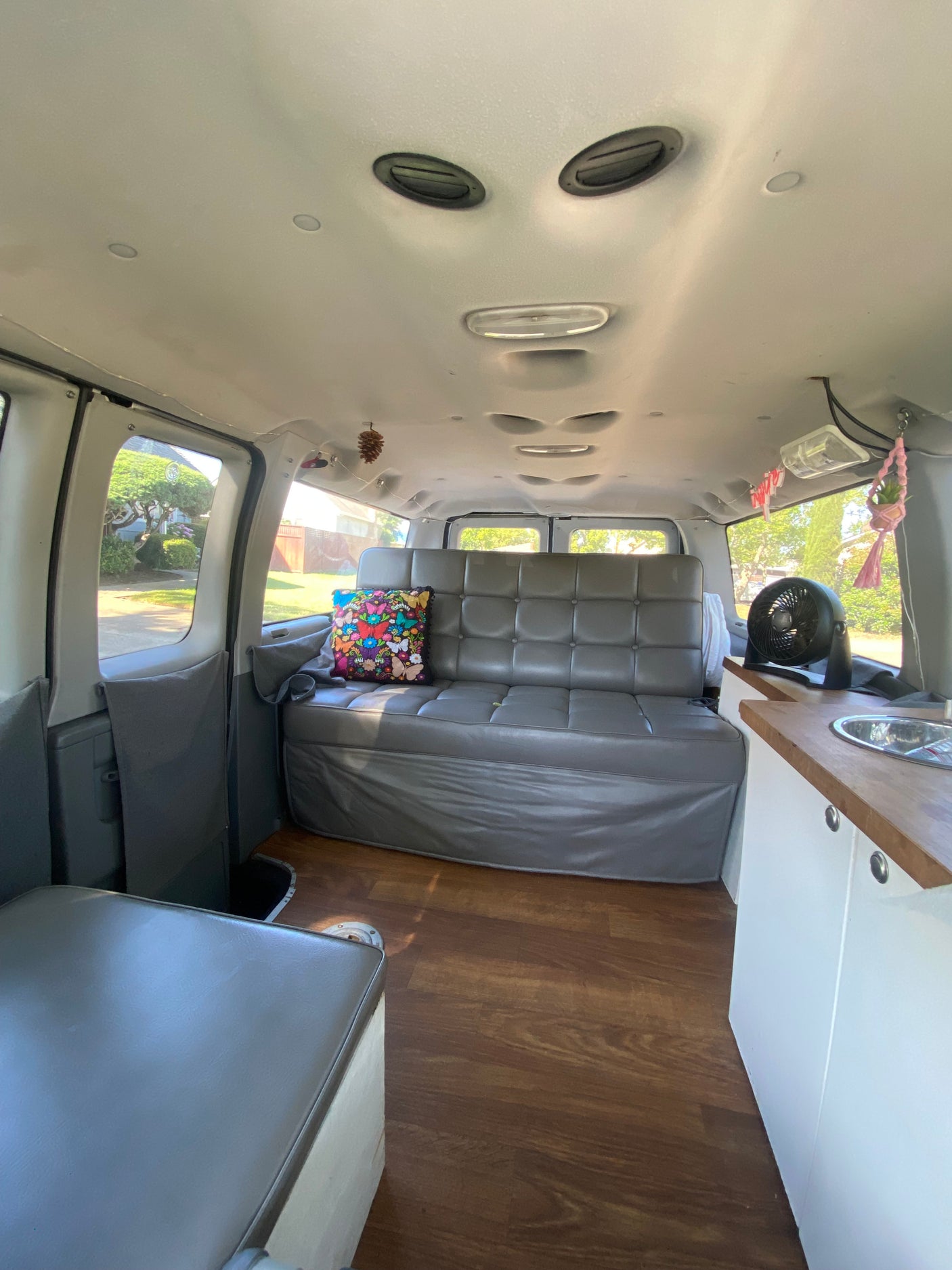 This rv rental interior features a gray sofa, wood-look floor, and a small kitchenette with a sink and fan.