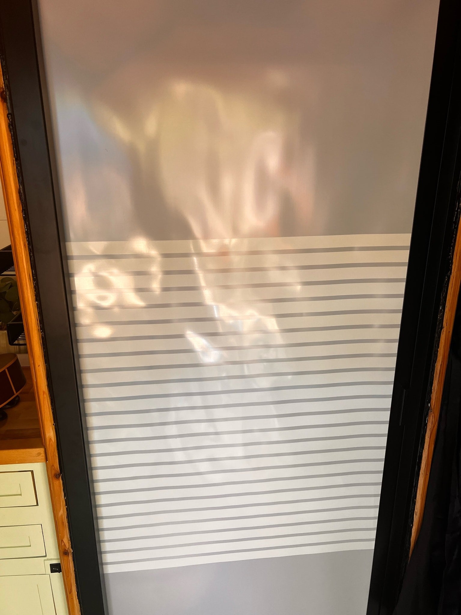 RV rental interior: A window features a two-tone blind; sheer top, striped bottom. Sunlight reflects warmly.