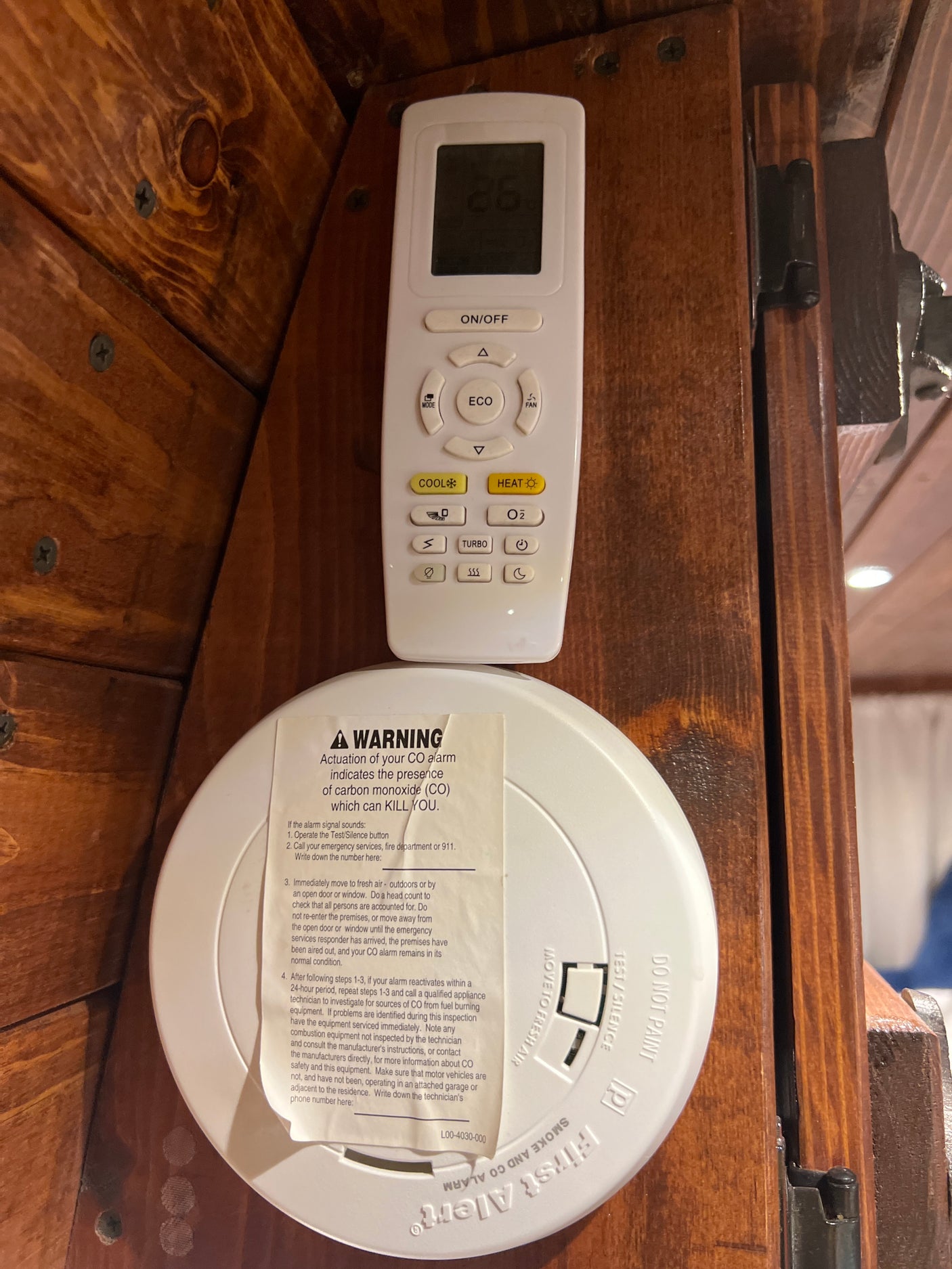 An RV rental interior shows a First Alert CO/smoke alarm with warning label below an air conditioner remote on a wooden wall.