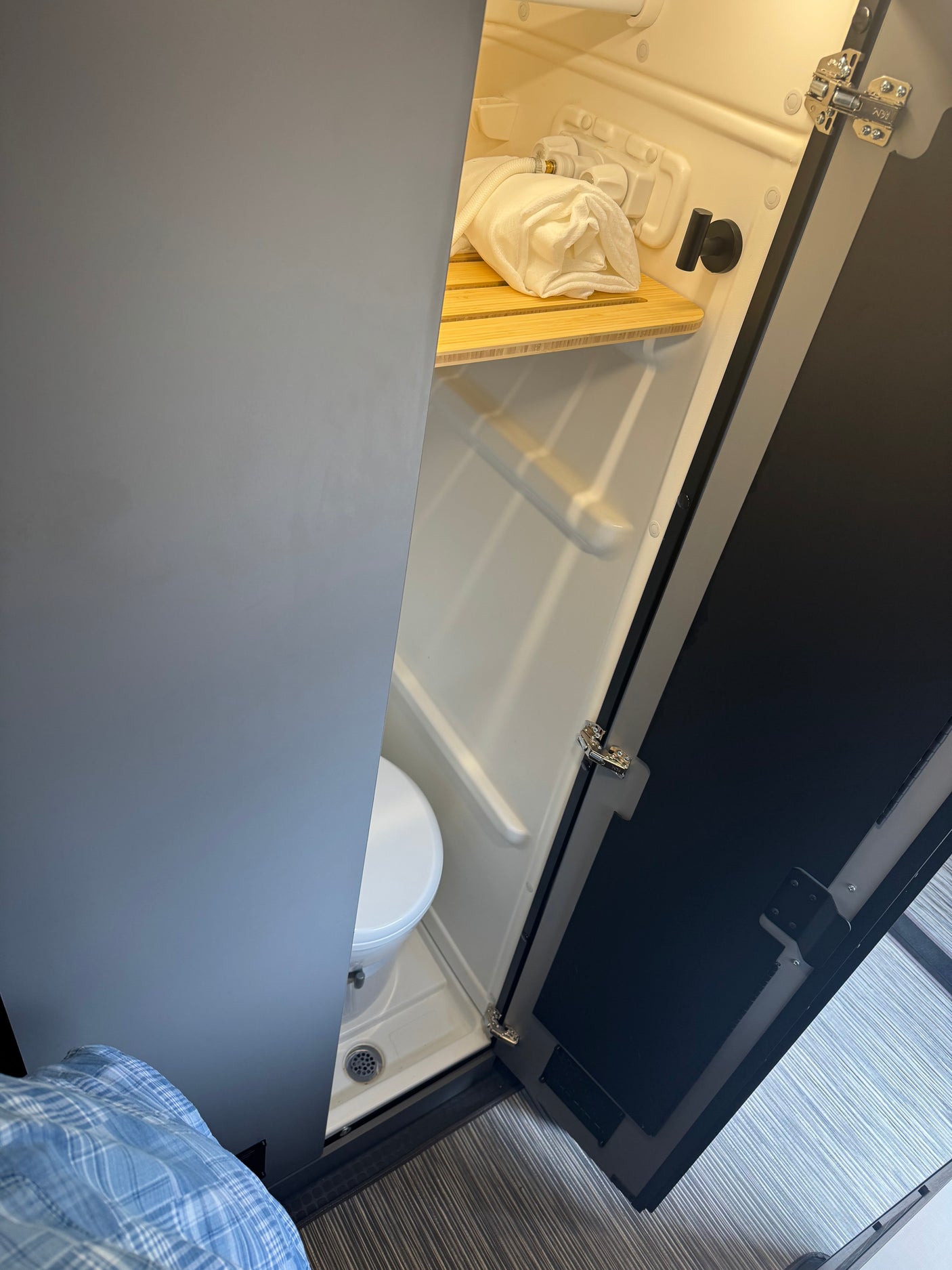 Compact RV rental bathroom featuring a shower, toilet, and a rolled towel on a shelf. Ideal for mobile living.