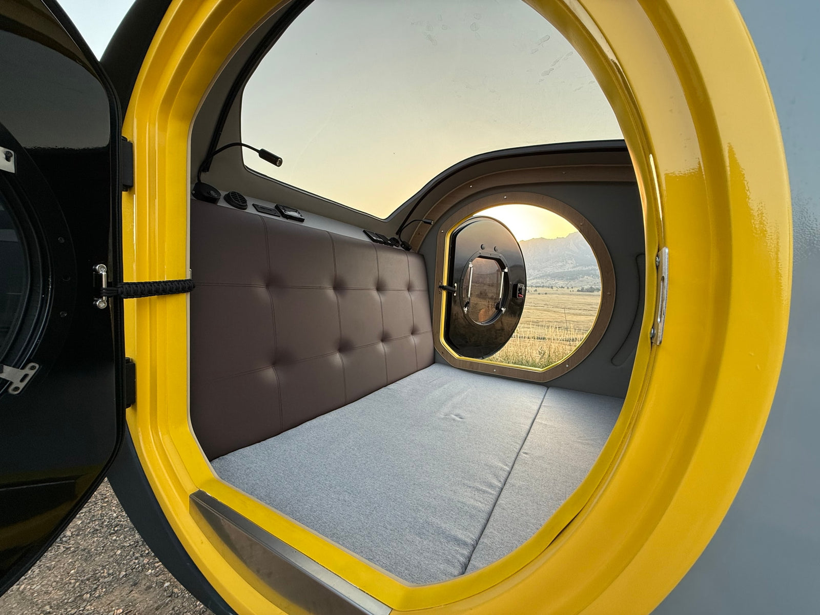 Cozy RV rental interior with bed, large windows, and scenic mountain view at sunset. Perfect for a road trip.