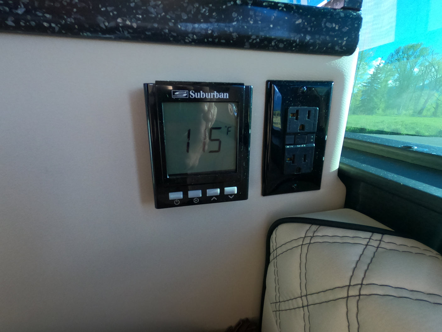Inside an RV rental, a digital thermostat displaying 15°F is next to an electrical outlet and cushioned seat.