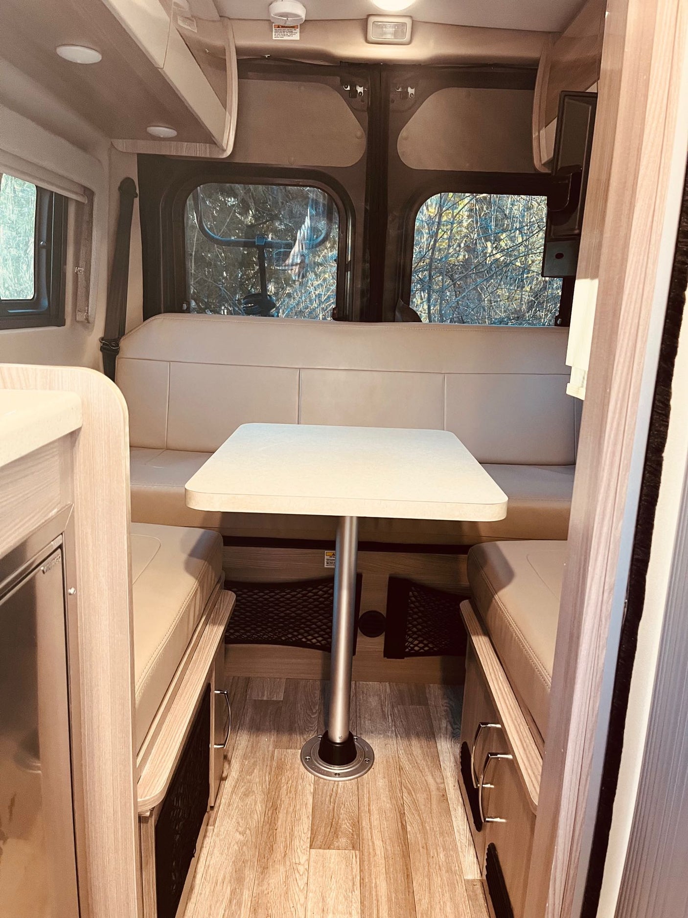 Cozy rv rental interior: A bright dining area with a table, light cushions, and scenic windows, ideal for travel.