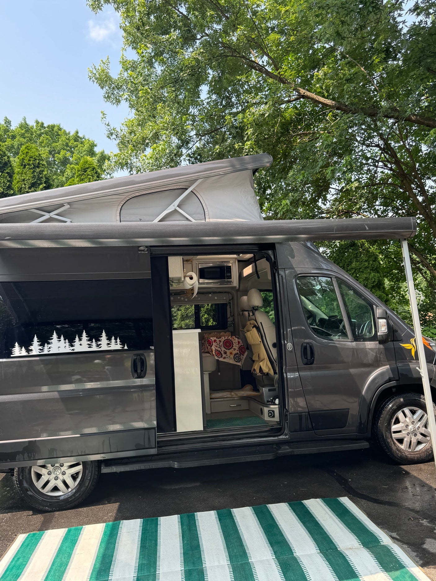 Spacious dark gray RV rental with a pop-top roof and open side door revealing a cozy interior, set up outdoors.