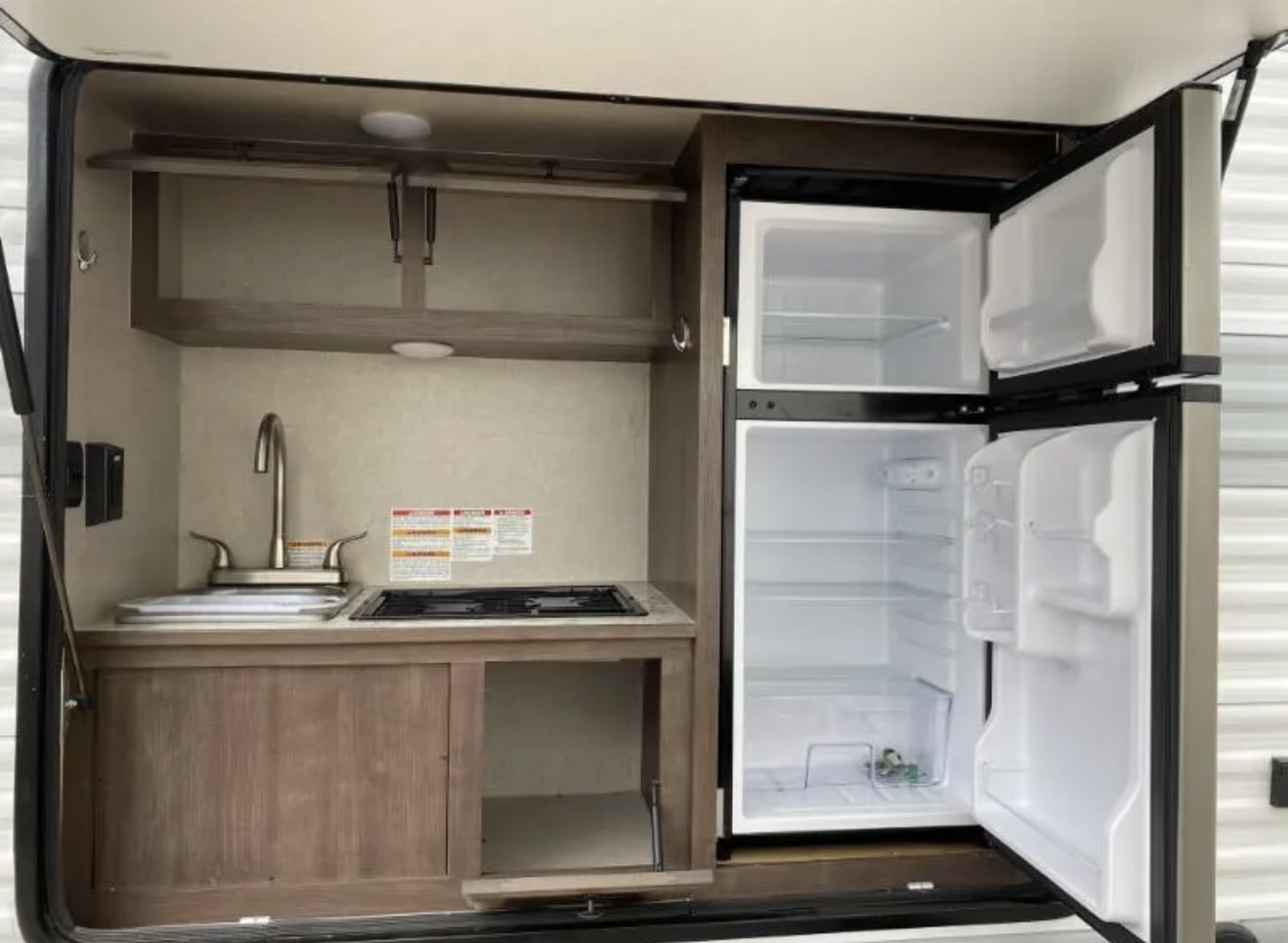 and view through the rear ramp door.|Rear view of an RV rental toy hauler with its ramp down and a black mesh screen covering the cargo area entrance.|This RV rental features a compact kitchen with a sink