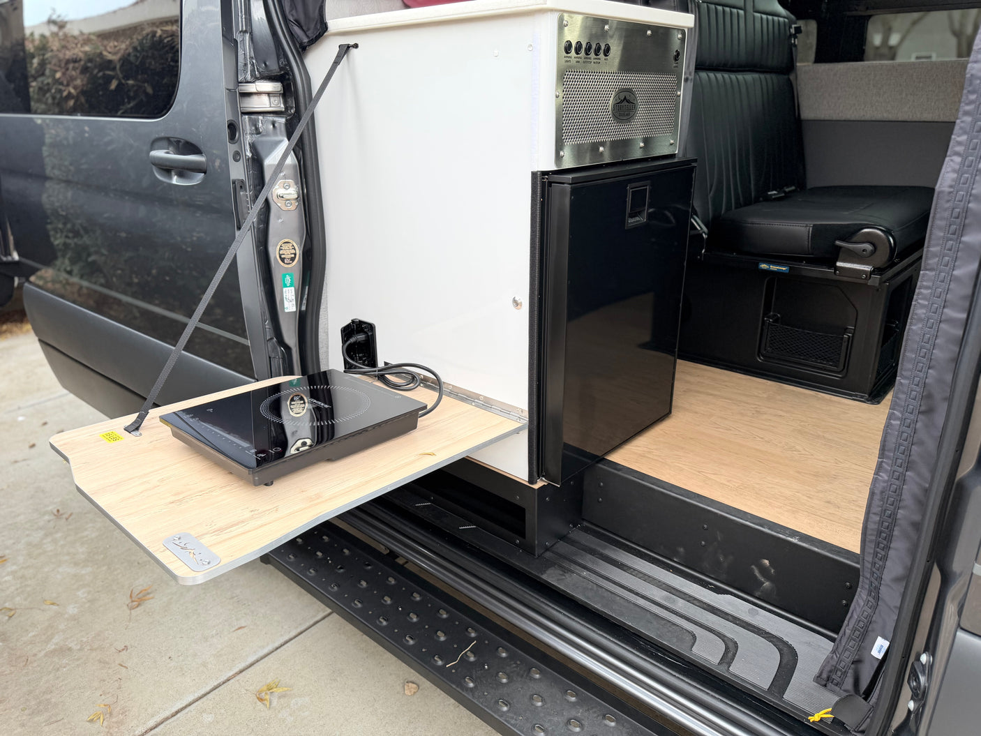 This RV rental features a Storyteller Overland camper van interior with a pull-out induction cooktop, fridge, and control panel.