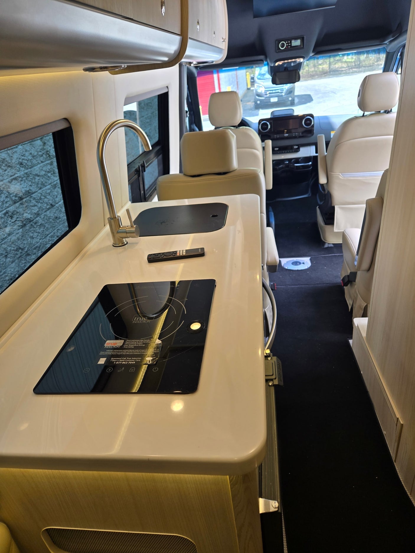 Step inside this RV rental! A modern kitchen area features an induction cooktop, sink, and faucet, leading to the light-colored front seats.