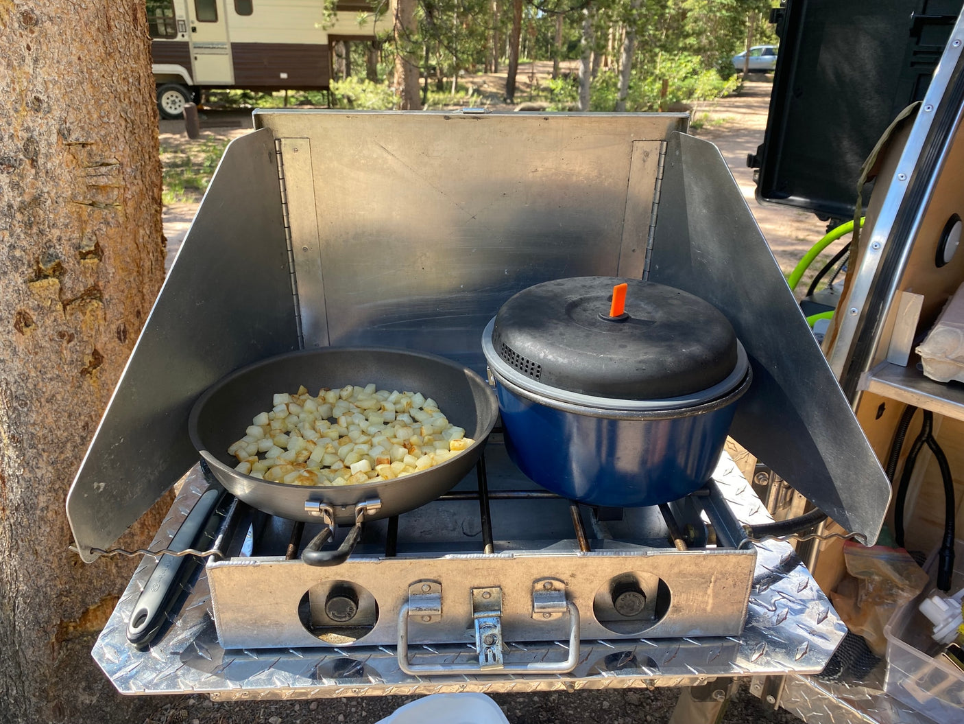 RV rental outdoor kitchen setup. Diced potatoes cook on a camp stove, next to a pot, preparing a delicious meal.
