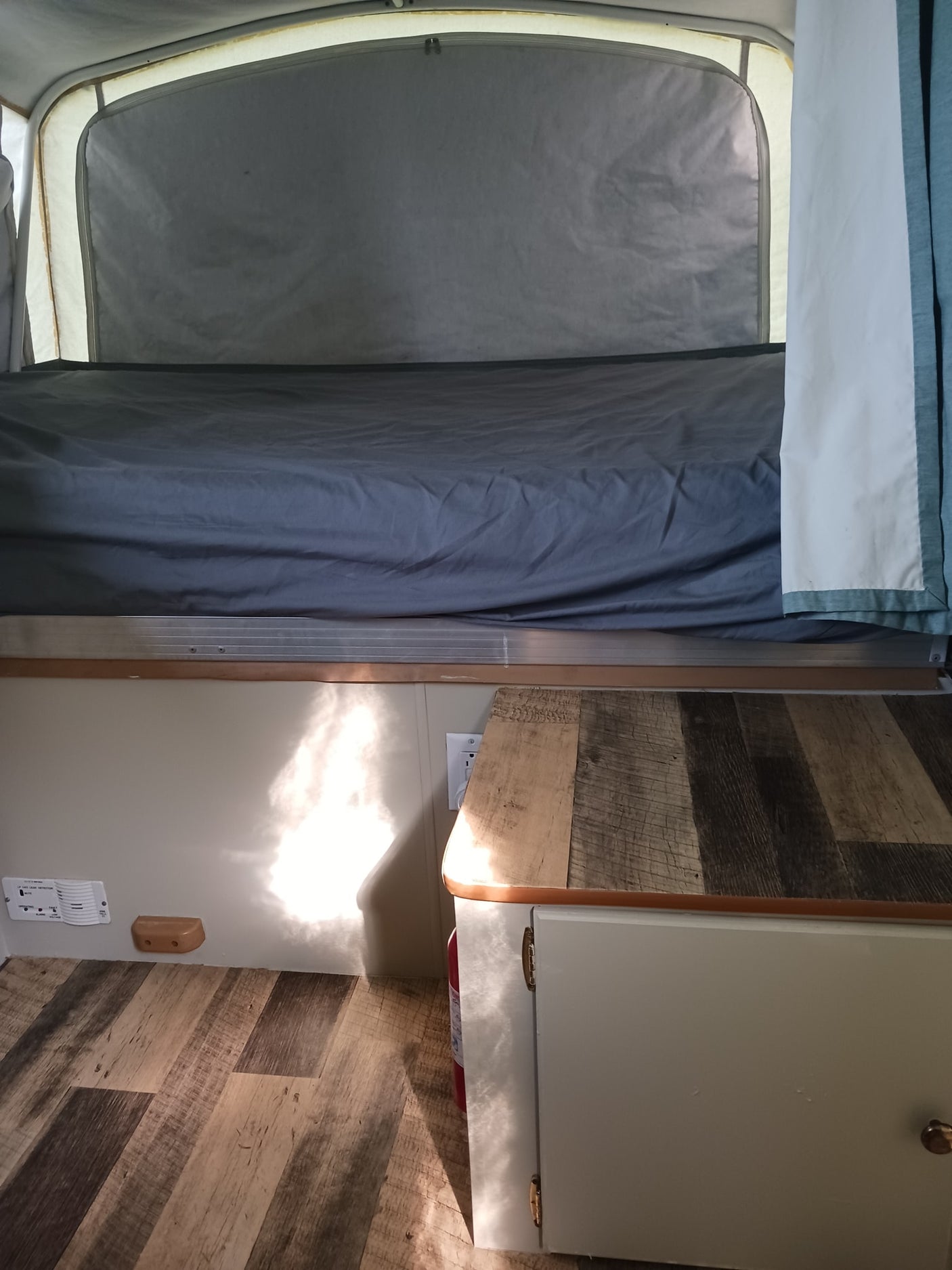 Cozy RV rental interior with bed, wood counter, and safety features like an LP gas detector and fire extinguisher.