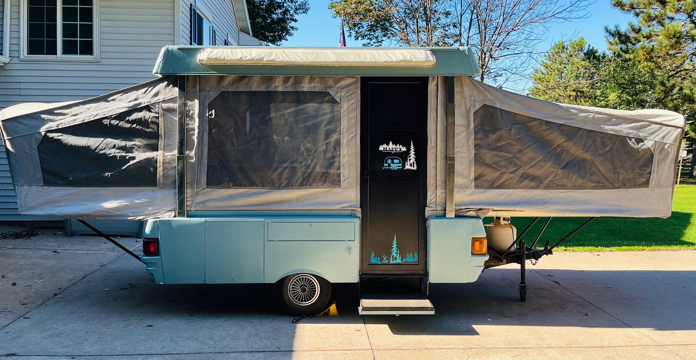 This fully set-up light blue pop-up RV rental is ready for adventure with its "HAPPY CAMPER" door.