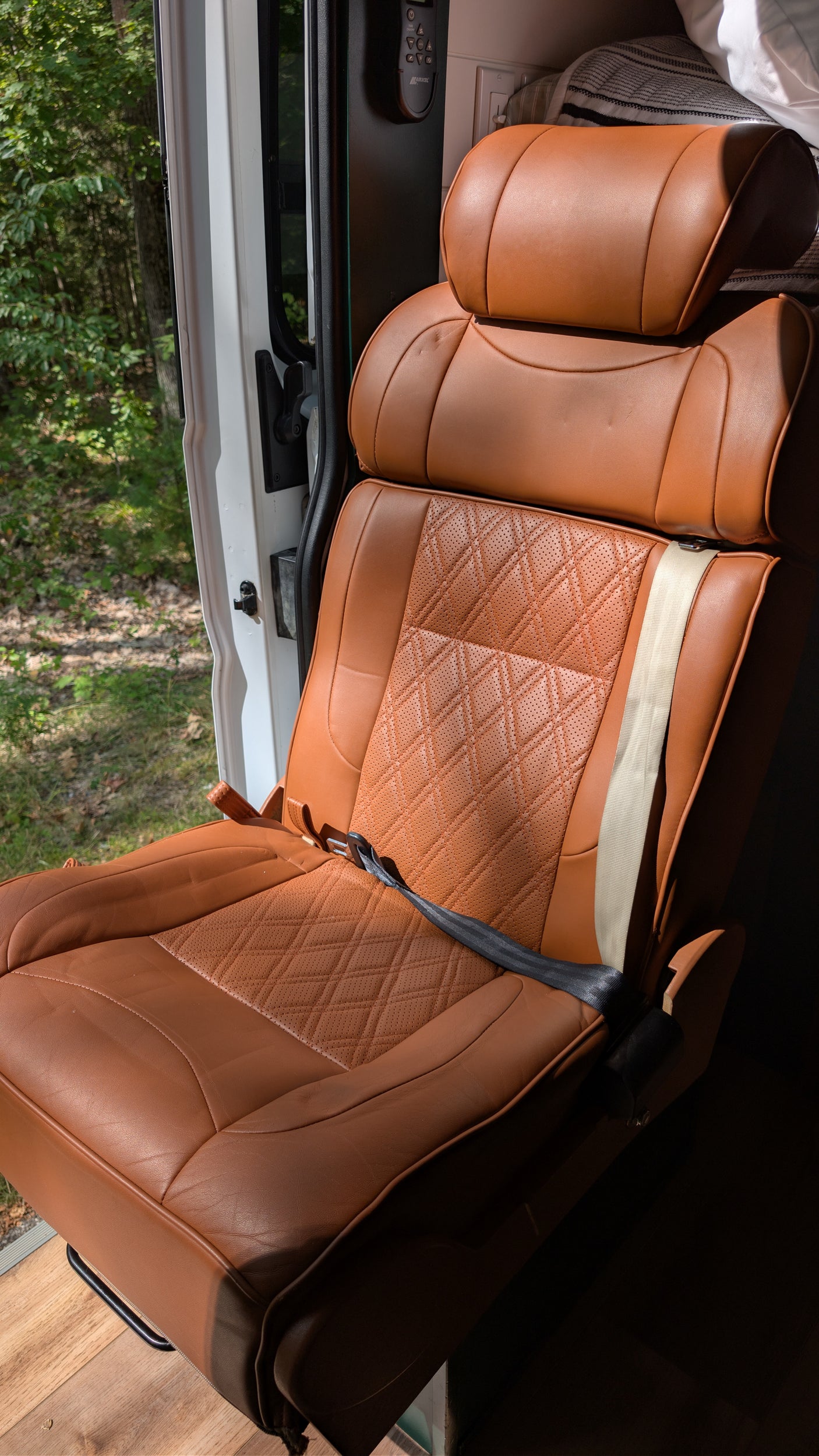Stylish brown leather seat in an RV rental, featuring quilted details. Enjoy comfortable travel with nature views from the open door.