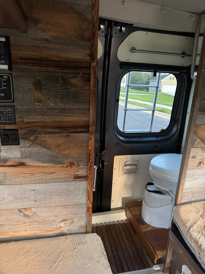 Explore this RV rental! Rustic wood interior, control panel, portable toilet, and cozy cushioned seating in a functional camper van setup.