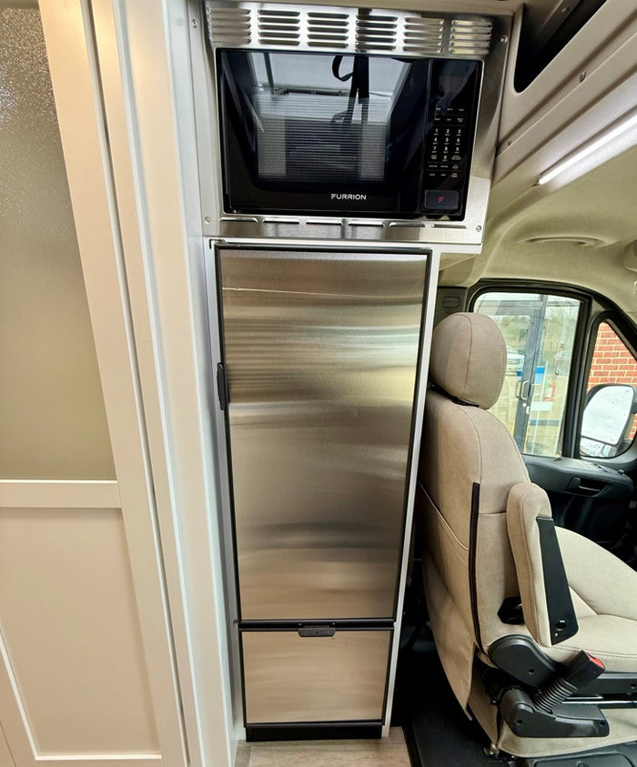 RV rental interior shows a compact stainless steel microwave over a refrigerator, next to a comfy driver's seat.