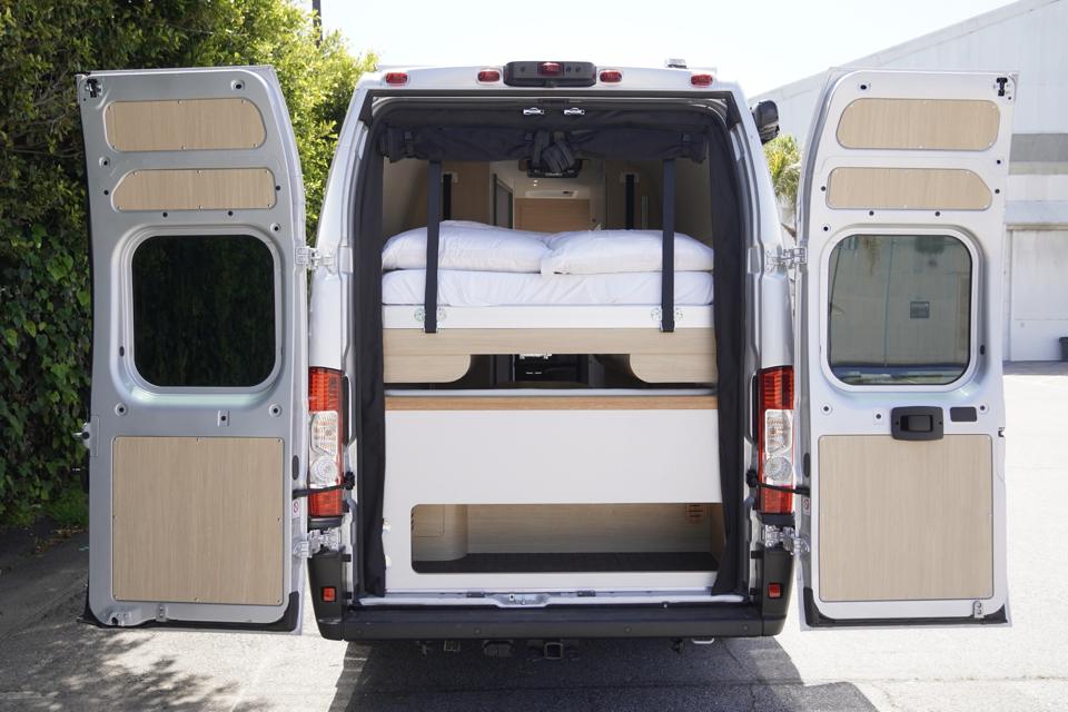 Rear view of an open white camper van with a cozy elevated bed & storage inside, perfect for your next rv rental.