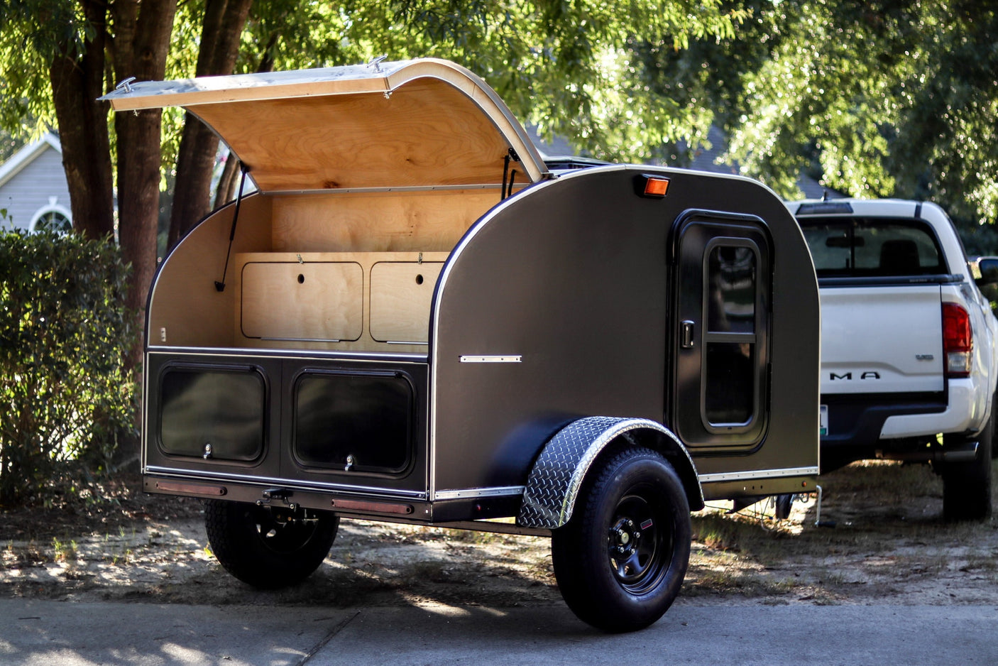 perfect for outdoor adventure.|A black teardrop camping trailer with an open wooden galley hitched to a truck