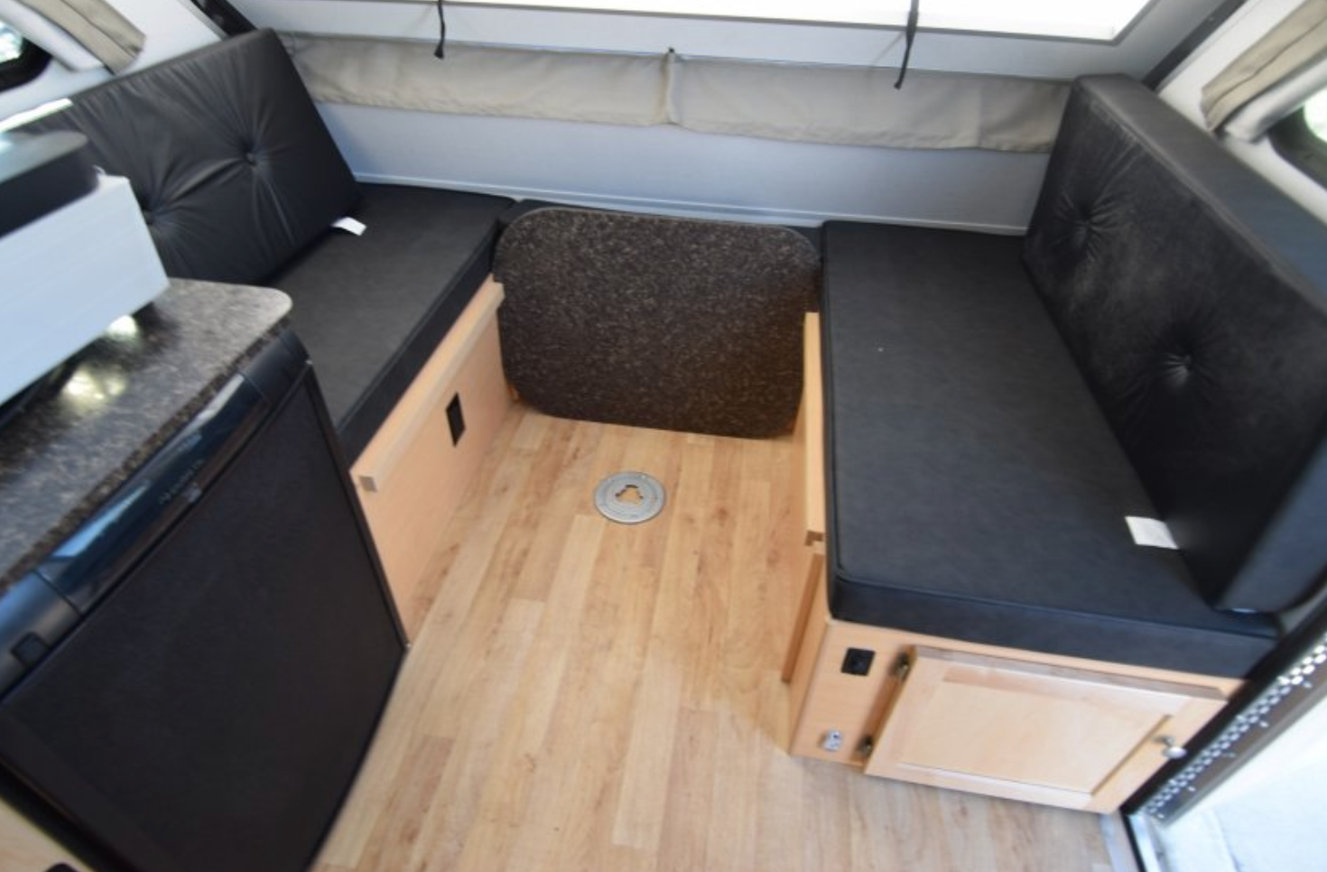 Compact rv rental interior: black dinette benches, light wood floor with table base, and compact kitchen/fridge. Ready for adventure.