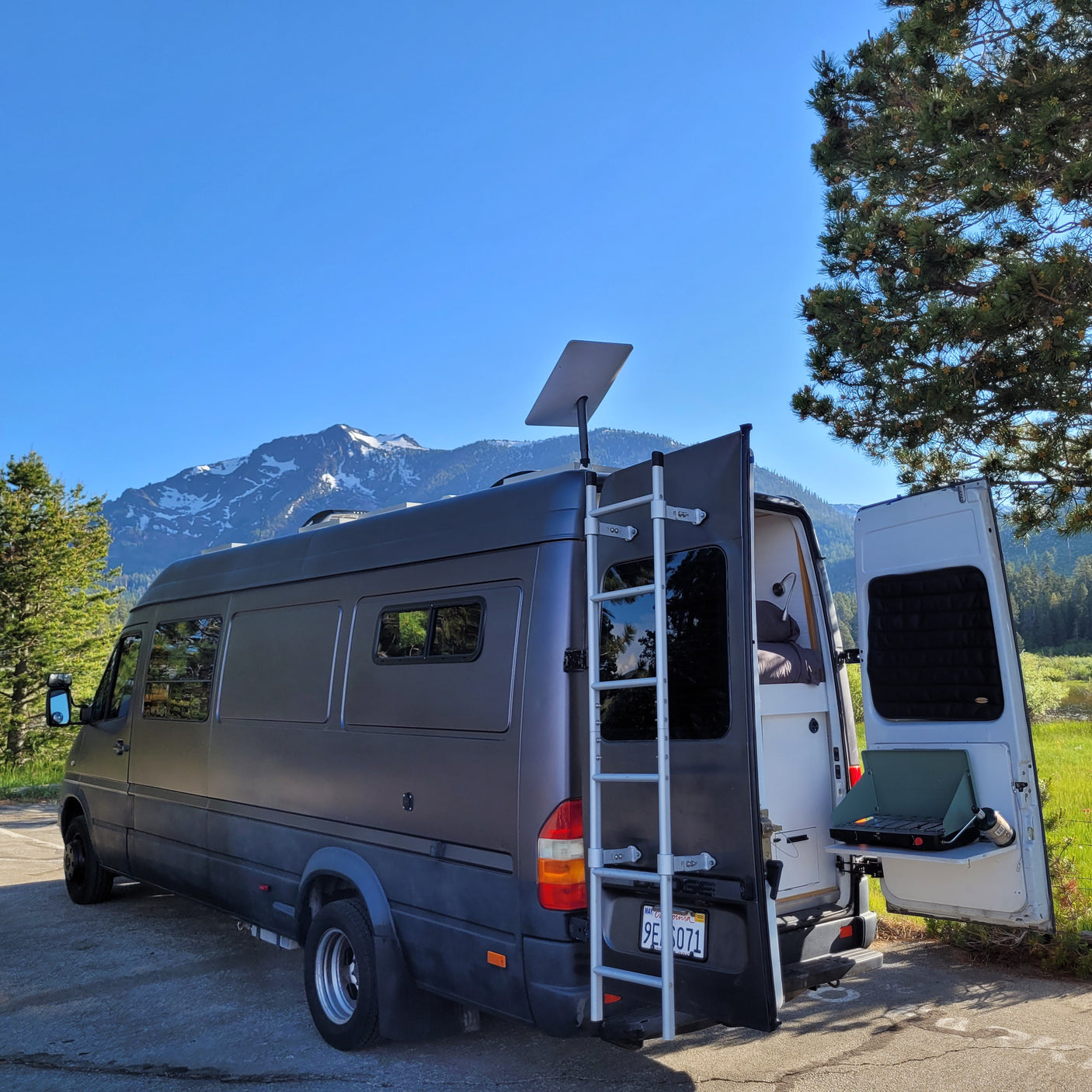 This RV rental camper van, parked amidst mountains, shows its open rear doors and equipped camping setup.