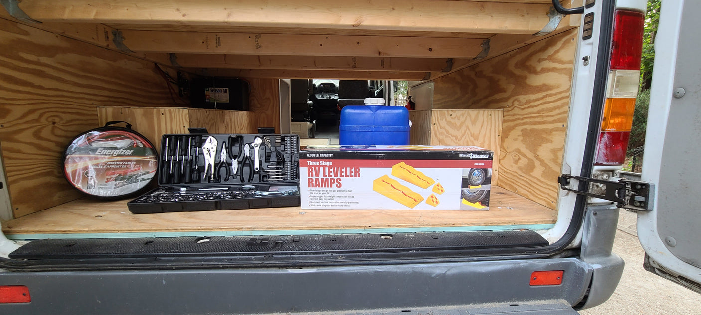 Prepped for RV rental adventures: Van's organized rear storage with tools, booster cables, water jug, and RV leveler ramps.