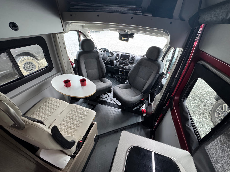 RV rental interior: Swiveling front seats face a dinette table with two red mugs, creating a versatile living space.