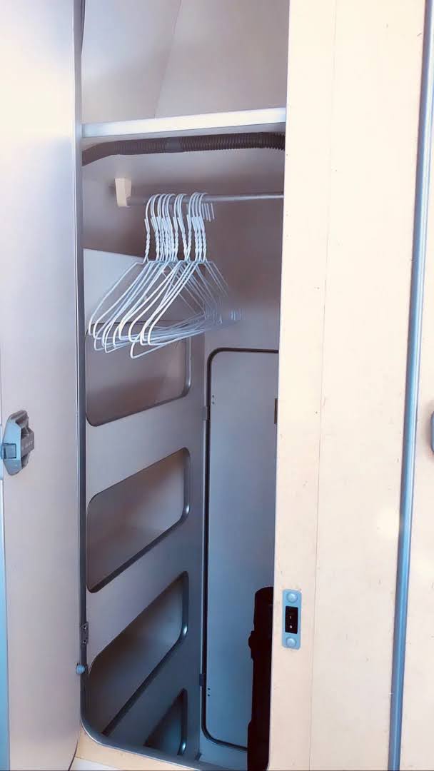 Open closet in an RV rental, with a metal hanging rod holding white wire hangers. It includes left-side shelves and a dark hose above. — photo 20