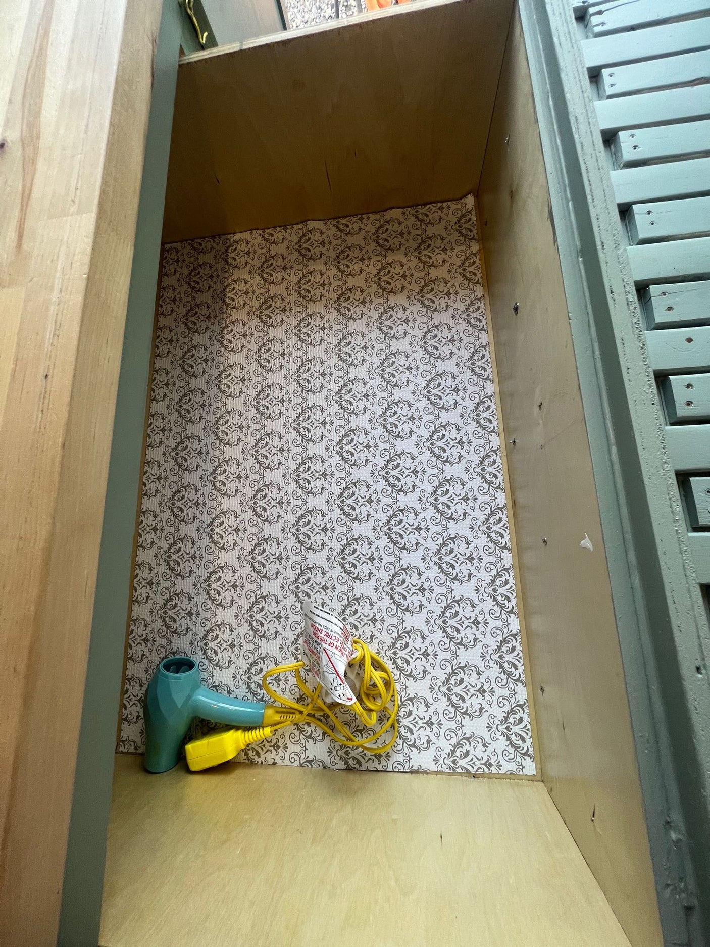 RV rental storage drawer, lined with patterned paper, holding a compact teal hair dryer & yellow cord.