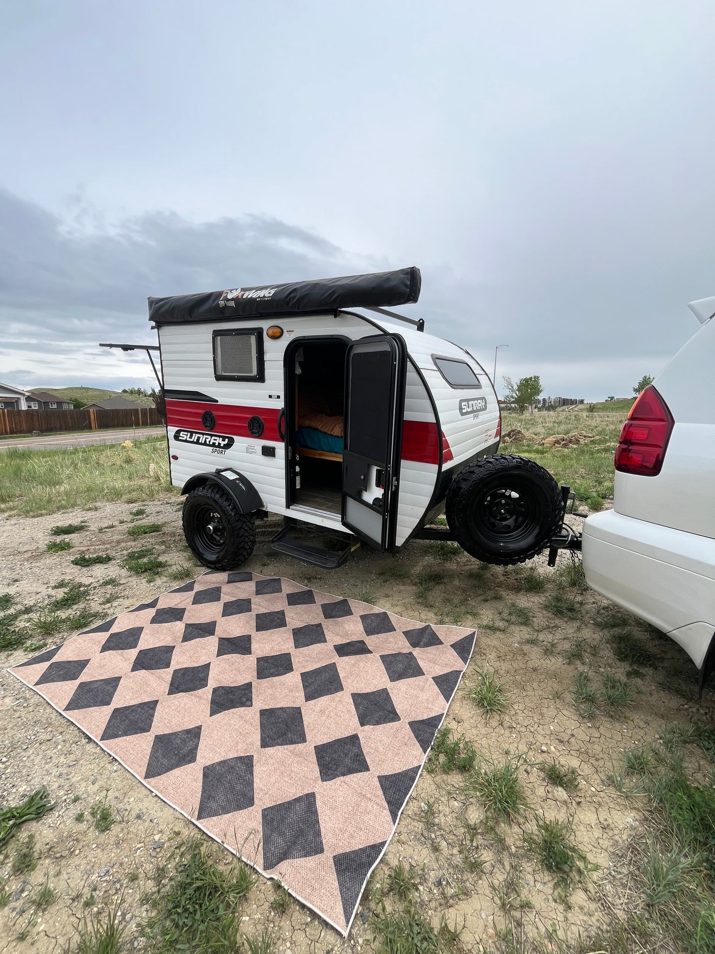 An RV rental: A small white & red teardrop camper hitched to an SUV, door open to a bed, next to an outdoor mat. — photo 8