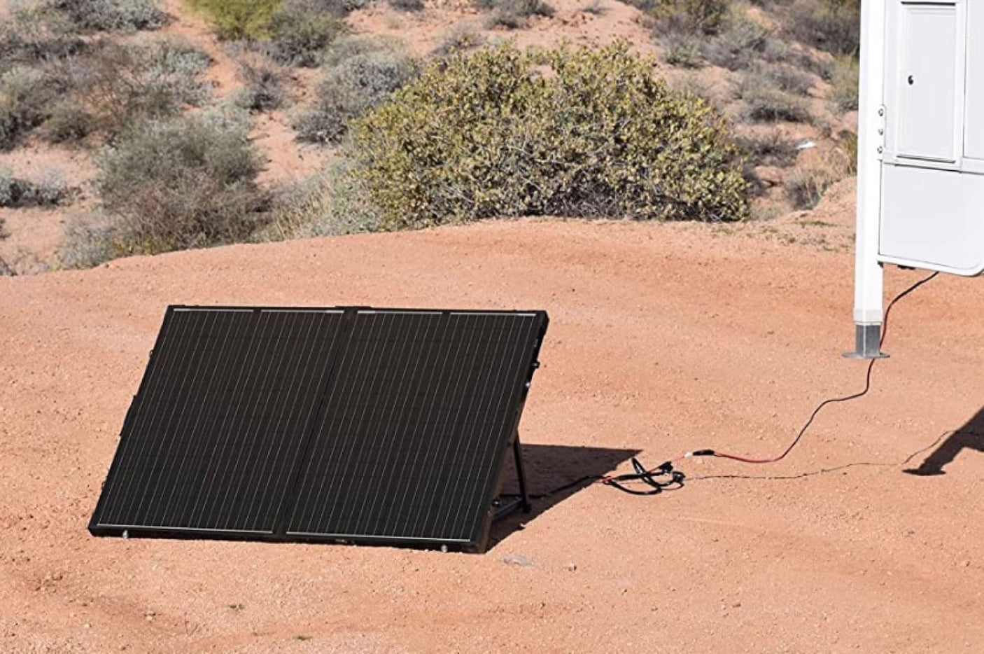 Portable black solar panel charges an RV rental in a desert camp. Ideal for off-grid power and sustainable RV adventures.