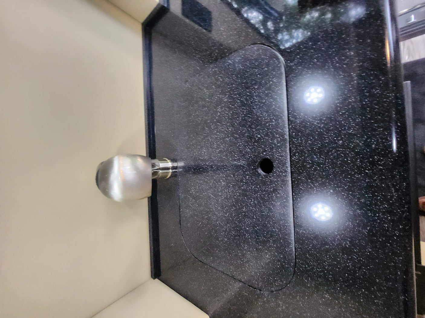 RV rental kitchen: Dark speckled countertop with a modern faucet, covered sink, and illuminated by bright LED lights.