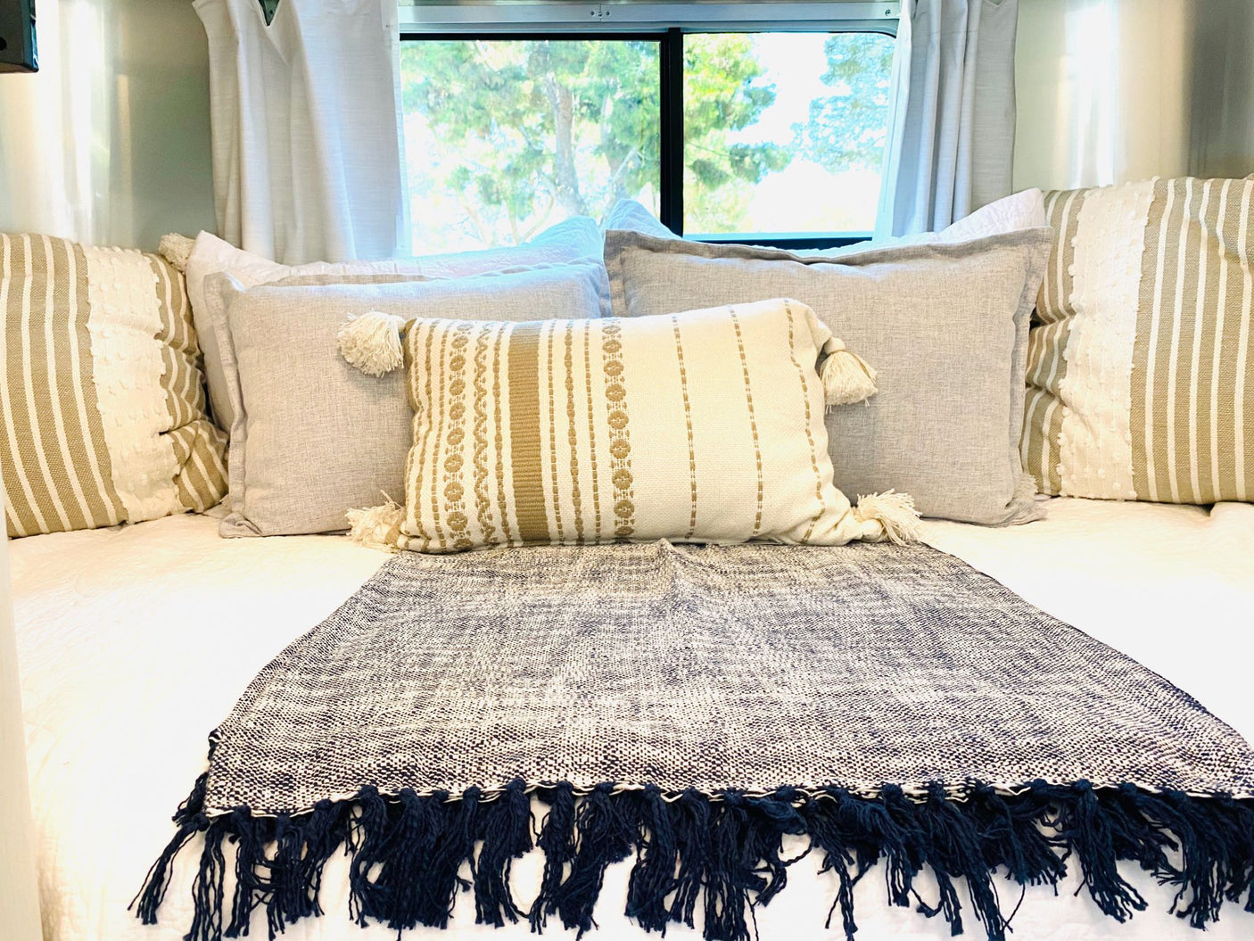 Cozy RV rental bedroom with stylish neutral pillows, patterned throw blanket, and scenic window view.