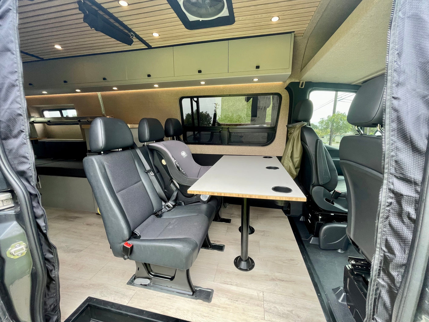 Interior of an RV rental with a dining table, passenger seating, and a child car seat in place.