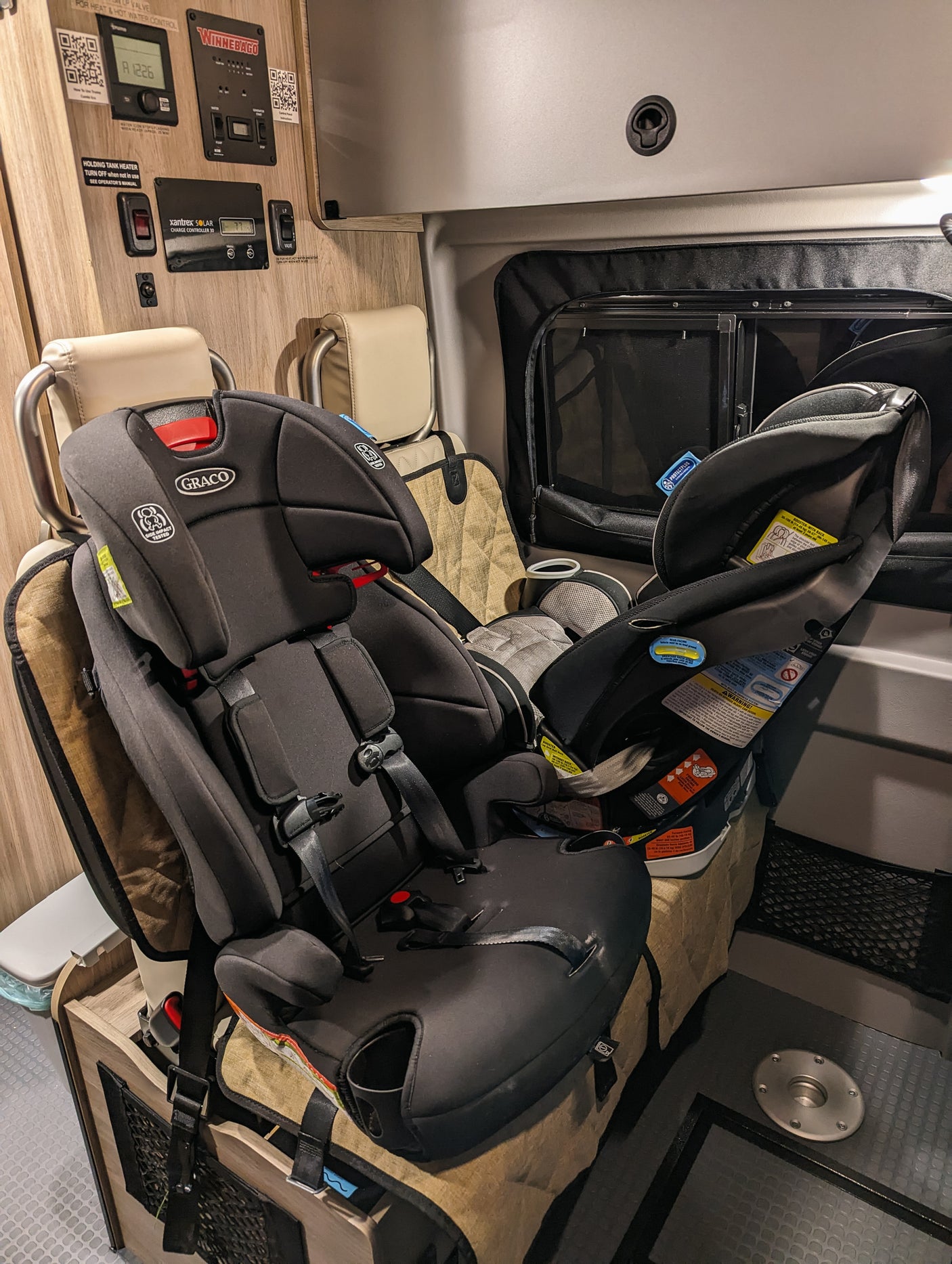 Inside an RV rental, two Graco child safety seats are ready for family adventures. Controls for Winnebago systems visible.